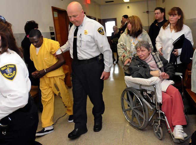 Sudbury Pines Extended Care resident Ruby McDonough, 63, in wheelchair at right, watches as Kofi Agana, 49, left, who she says sexually assaulted her last year while Agana was an employee at Sudbury Pines, leaves Framingham District Court after a hearing Tuesday.  Judge Robert Greco ruled that McDonough, who has been diagnosed with expressive aphasia and had previously been ruled incompetent to testify, will be allowed to testify at trial.