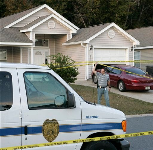 A Tallahassee investigator lifts police tape to pass under at a home where a woman and three children were slain on Saturday, Nov. 20, 2010 in Tallahassee, Fla. A woman and three young children were found killed at a violent crime scene in a north Florida home on Saturday, and homicide detectives were out looking for whoever might have had a reason to harm them, police said.