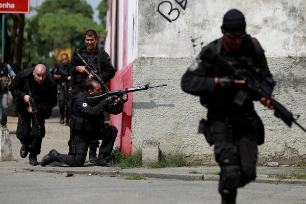 A POLICEMAN runs for cover as another one aims his weapon during an operation against drug traffickers in Vila Cruzeiro, Brazil, on Thursday.