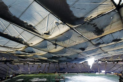 AP Photo/Ann Heisenfelt 
Snow falls into the field from a hole in the collapsed roof of the Metrodome in Minneapolis Sunday. The inflatable roof of the Metrodome collapsed Sunday after a snowstorm that dumped 17 inches on Minneapolis. No one was hurt, but the roof failure sent the NFL scrambling to find a new venue for the Vikings’ game against the  Giants.