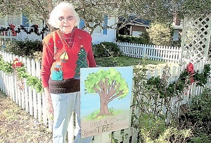 Audrey Robbins poses with a sign she has posted on the front of her home on Markland Place in St. Augustine calling on the city commission to save a 100-year-old tree growing on a lot behind her home. By PETER WILLOTT, peter.willott@staugustine.com