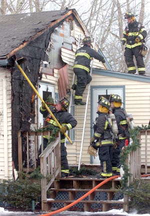 Raynham firefighters investigate the side of the house where a house fire started at 203 Hall St. in Raynham on Dec. 25. The homeowner is Jean Eaton, who was home at the time of the fire.