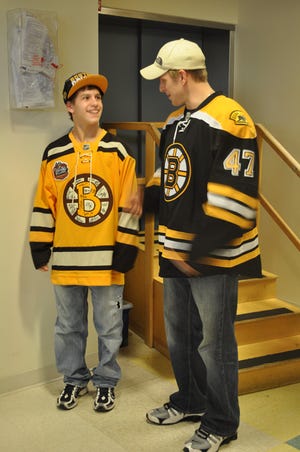 Milford High School hockey player and Blackstone-Millville High School student Tyler Symes, left, talks with Bruins player Steven Kampfer.