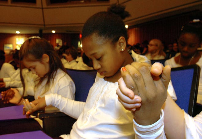 Baker School students Melissa Millien, 10, and Bayleigh Westerlund, 10, hold hands during the invocation at a Martin Luther King Jr. Day event at Massasoit Community College in Brockton on Monday, Jan. 17, 2011.