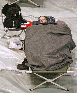 A man sleeps in a shelter step up by the American Red Cross at the Canton Memorial Civic Center Thursday. Single men and single women have there own sides of a curtain to sleep on.