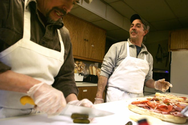 Ralph Poness, right, of Framingham looks on as Evan Ewing of Medford quickly cuts up pickles for an order of 4 Philly style hoagies on Sunday at the Mount Hollis Masonic Lodge in Holliston. Poness and Ewing, Masons at the lodge who created over 100 sandwiches on Sunday have been making the sandwiches every Superbowl Sunday for the last 19 years to benefit the Holliston Food Pantry and the Angel Fund.