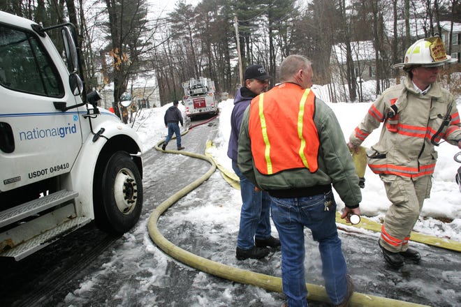 Franklin Deputy Chief Paul Sharpe, right, moves a hose out of the way to clear room for an electric truck to shut off electricity to the home at 3 Rachael Dr. in Franklin on Tuesday after a small fire in the basement damaged an electrical panel and a water pipe. No one was hurt in the incident and the cause of the fire is still under investigation. Franklin Water Dept. workers Steve Carlucci and Jaybird look on. Jacob Belcher/ Milford Daily News and Wicked Local