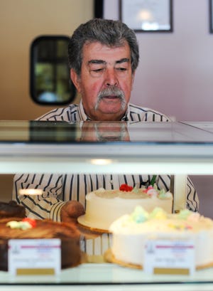 Arthur Cabral, owner of Art’s Bakery in Raynham, rearranges cakes on display.