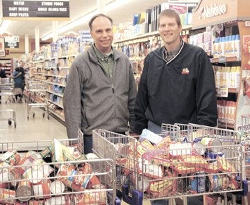 Mark Heil, left, and Matt Jacobs show off their grocery items following a two-minute shopping cart race at Dave’s Supermarket as part of Food Check Out Week.