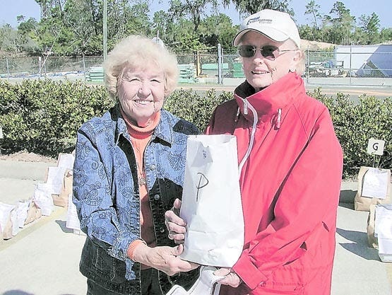 Pilot member Jeanette Smith, left, gives caladium bulbs to Shirley Green who purchased tubers that will produce pink leaves. Shirley plans to put the bulbs in planters outside a gate at her home.