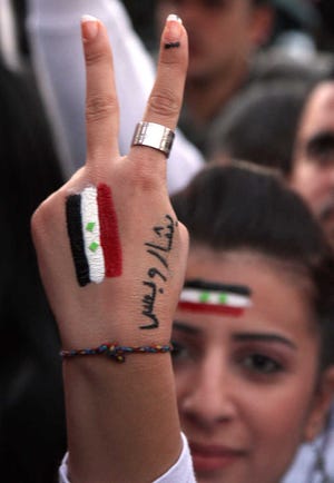 A supporter of Syrian President Bashar Assad flashes the V sign with the Syrian flag and Arabic words “Only Bashar” on her hand in Damascus, Syria, Saturday.