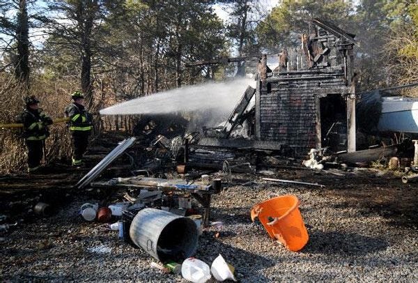 Firefighters extinguish a fire that destroyed a barn Monday behind a home at 28 High Bank Road in South Dennis.