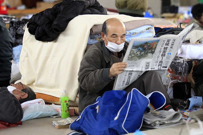 An evacuee reads a newspaper yesterday in a high school gymnasium turned into an evacuation center in Watari, Miyagi Prefecture.