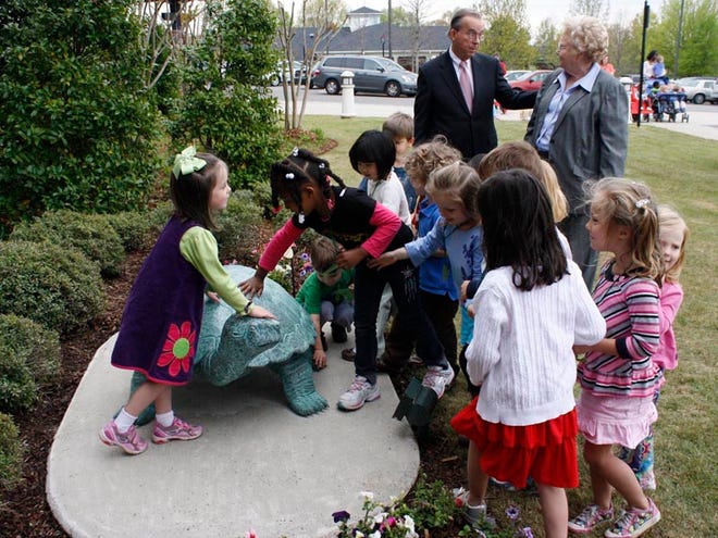 Students welcome “John,” the tortoise statue sculpted by Frank Fleming and given by Ann Rhoads, to the garden in front of the University of Alabama Child Development Research Center as University of Alabama President Robert Witt and Rhoads talk behind them.