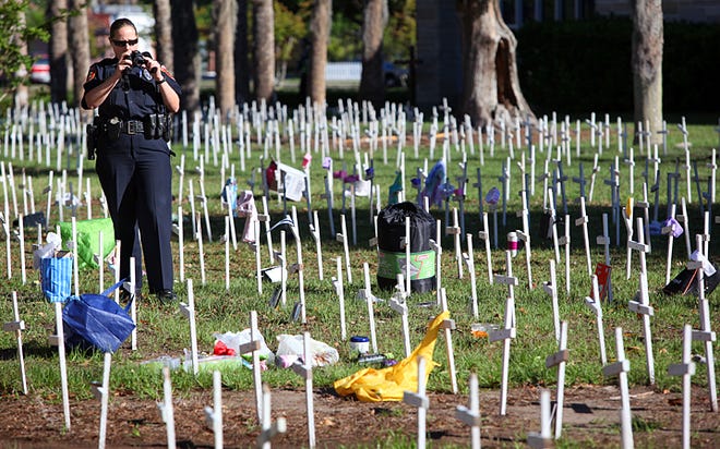 St. Augustine Police officer Alina Shirshikova takes photographs of clothing, household items and trash that were placed on and around the 4,000 crosses that blanket the grounds at the Prince of Peace Church at the Mission of Nombre de Dios on Wednesday morning. By DARON DEAN, daron.dean@staugustine.com