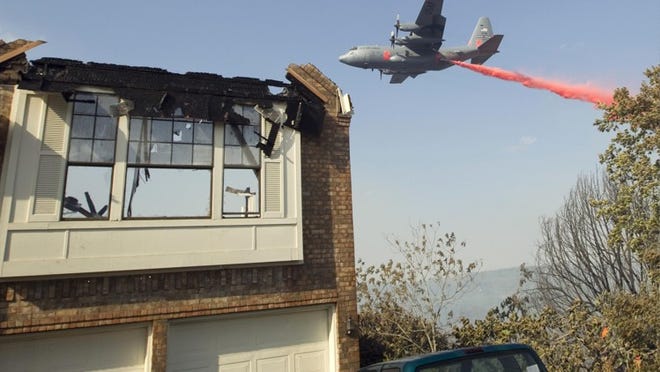 A Texas Forest Service C-130 airplane drops red-tinted fire retardant near a home on Callbram Lane in Oak Hill. Officials evacuated hundreds from the area, and no injuries had been reported from the blaze, which spread to about 100 acres Sunday afternoon.
