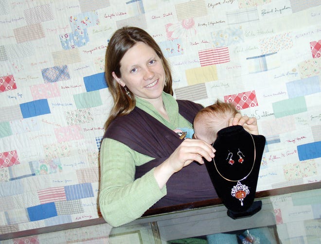 East Bloomfield silver smith, Beth Altemus, of Main Street, with her 4 and a half month old, Emilia Hayes, adjusting a necklace and earring set she designed using carnelian set in Sterling silver with a filigree pattern she created