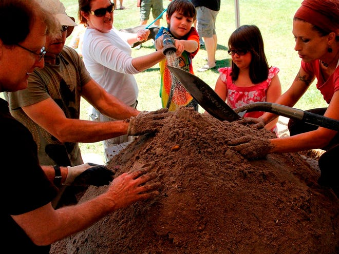 Jasen Winn, 8, center, sprays water onto a mound of dirt that is being formed by members of the Devotional Eco Villages International Project into a mold, which will have “cob” laid over it that will then form an earth oven for cooking, during the kickoff party for the 2011 Eat Local Challenge held at Kumarie's Organic Garden in Alachua on Sunday.