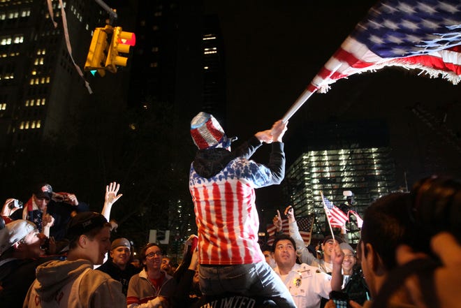 Perched on another's shoulders, Ryan Burtchell, of the Brooklyn borough of New York, center, waves an American flag over the crowd as they respond to the news of Osama Bin Laden's death early Monday morning May 2, 2011 by ground zero in New York.  President Barack Obama announced Sunday night that Osama bin Laden was killed in an operation led by the United States. (AP Photo/Tina Fineberg)