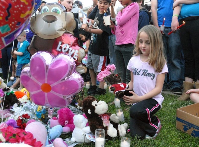 Seven-year-old Zoey Speaker lays a teddy bear and flowers onto the pile of gifts at the Souderton Gardens apartment complex on Tuesday night in memory of Skyler Kauffman who was killed there on Monday.