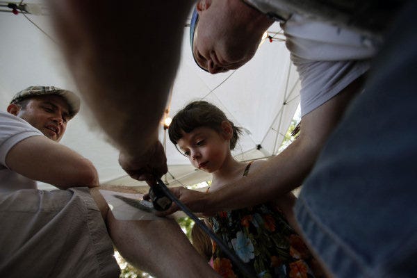 Four-year-old Sarah Jacobs, middle, watches as Doyle Heck, right, of Heck Graphics, gives her dad, Noel Jacobs, an airbrush tattoo during the 2010 Edmond Jazz and Blues Festival. Oklahoman Archive photo by Miranda Grubbs MIRANDA GRUBBS