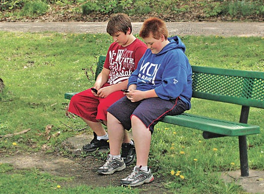 Josh Gerrie, 12, and Tanner Reattoir, 13, took advantage of a park bench to rest a bit after some hard biking and catch up with their friends through text messaging. The duo, reports indicate, had stopped at the makeshift park to engage in electronic communication, because it’s illegal to text and drive.