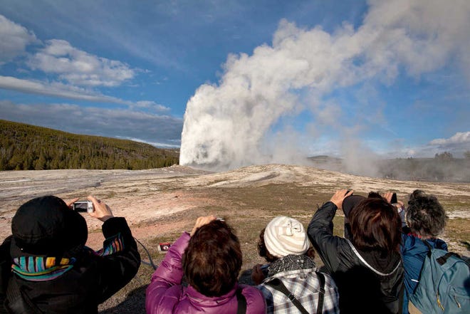 Tourists photograph Old Faithful erupting on schedule in Yellowstone National Park, Mont. As the summer travel season kicks off, many people may take one look at the price of an airplane ticket or a gallon of gas and decide to put off their dream vacation for one closer to home and closer to nature.