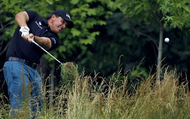 Phil Mickelson hits out of the tall grass along the 14th fairway during the first round of the U.S. Open on Thursday. He shot a 3-over 74 and is nine strokes behind leader Rory McIlroy.
