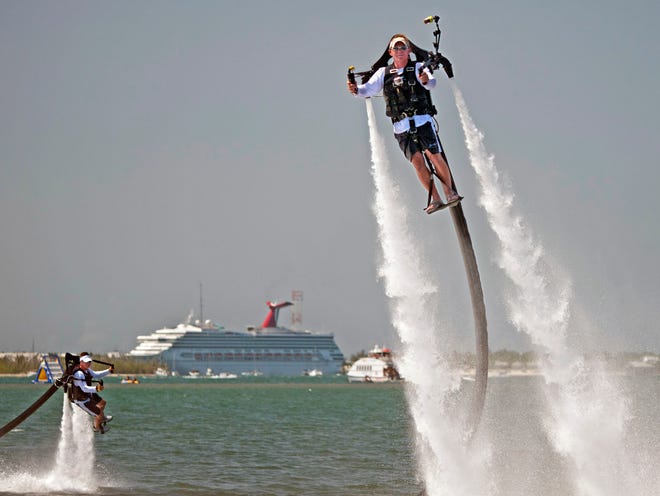 In this June 24, 2011, photo released by the Florida Keys News Bureau, Scott Oosting, left, and Dave Tuxbury, right, fly in Key West, Fla., with a new Florida Keys visitor offering called Jetpack Adventures providing human flight experiences. The flight apparatus is tethered by a 30-foot hose dragging a tiny boat with a pump that uses seawater as propellant. During training, the instructor remotely operates the vehicle, but as the participant becomes more proficient, he gains more control. (AP Photo/Florida Keys News Bureau, Rob O'Neal)