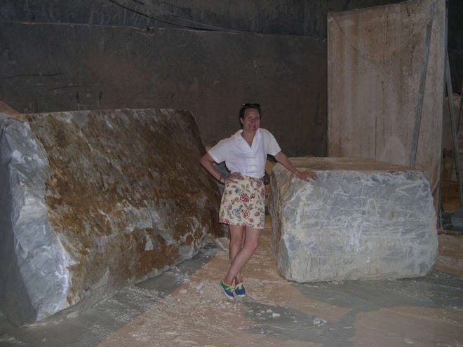 Laura C. Johnson stands in the bowels of an Italian marble quarry, leaning against a discarded marble block with marble mud at her feet.