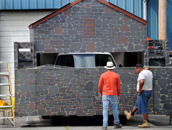 J.P. Bartlett workers Alfredo Alonso, right, and Pablo Davila check out their wholesale greenhouse company's Fourth of July float Friday in Sudbury. The float, a reproduction of the Wayside Inn's Grist Mill, celebrates the 100th anniversary of J.P. Bartlett.