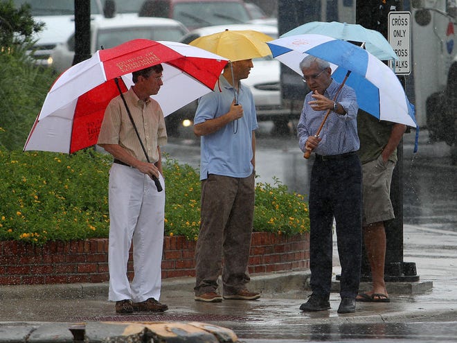 A group of people wait to cross SW 13th Street under umbrellas Friday, July 8, 2011.