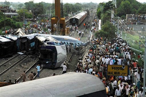 People gather around the wreckage of the Kalka Mail passenger train which derailed near the town of Fatehpur in Uttar Pradesh state, India, Sunday, July 10, 2011. The packed train was on its way to New Delhi from Howrah, a station near Kolkata, when its 12 coaches and the engine jumped the tracks. Dozens of people died and more than 100 are injured, according to officials.