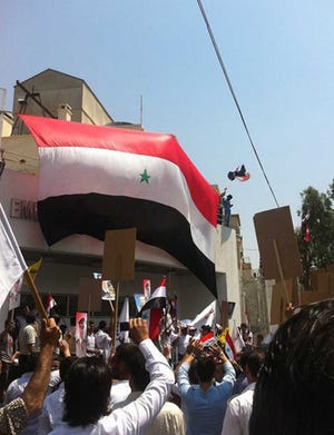 In this photo released by a Syrian news website Shukumaku and according to them, pro-Syrian President Bashar Assad protesters, hang a huge Syrian flag at the entrance of the US the embassy compound as they protest against the US Ambassador Robert Ford after his visit on Friday to the Syrian city of Hama, in Damascus, Syria, Monday, July 11, 2011. A U.S. official says the Obama administration will formally protest an attack on the American Embassy in Syria and may seek compensation for damage caused when a mob breached the wall of the compound before being dispersed by Marine guards.(AP Photo/Shukumaku Syrian News Website) EDITORIAL USE ONLY