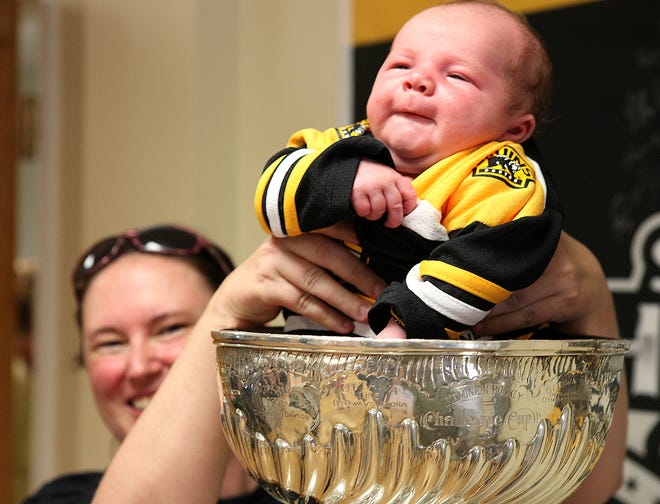 Four-week-old C.J. Davoe is held in Lord Stanley's Cup by Jill Otero of Marlboro during a viewing held at Sports and Physical Therapy Associates in Norwell on Monday. The Stanley Cup paid a visit to Norwell thanks to Bruins trainer, Scott Waugh, who now has a championship with both the Bruins and the Red Sox.