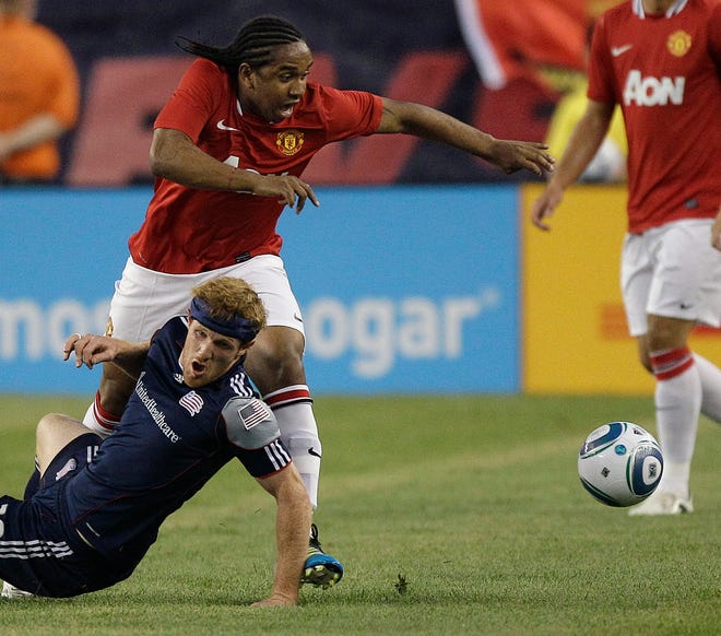 Manchester United midfielder Anderson takes the ball past a falling New England Revolution midfielder Pat Phelan, bottom, during the first half of their exhibition soccer match Wednesday in Foxboro.
