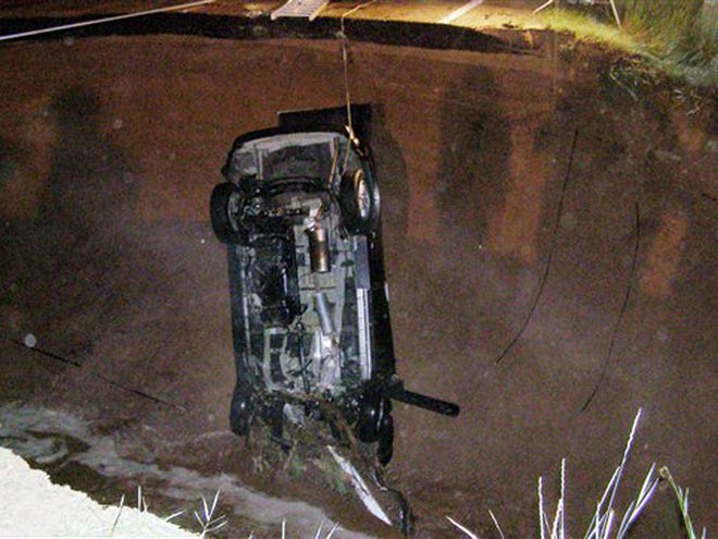 This image provided by the Utah Highway Patrol shows the wreckage of a car that ran into a hole, after heavy rain caused the collapse of State Road 35 that opened up a hole 40 feet wide and more than 30 feet deep.