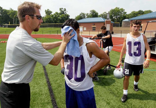 Head athletic trainer Eric Claas, left, applies a cold towel to sophomore Cuong Nguyn (30) during a Wednesday morning practice at Father Ryan High School in Nashville, Tenn. With the summer heating up, schools are trying to keep their student-athletes off the field during the hottest parts of the day by rescheduling practices and scrimmages.