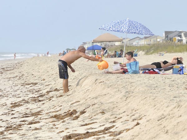 Monty Freeman reaches over Kure Beach's erosion escarpment to help his son C.T. with his sand castle dreams while his wife Shari enjoys the sun while spending a week on vacation.  PHOTO BY JEFF JANOWSKI/WILMINGTON STARNEWS