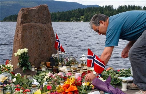 A man places a Norwegian flag between flowers in Utvika in front of the Utoya island, near Oslo, Norway, Tuesday, July 26, 2011, where a gunman Anders Behring Breivik killed at least 76 people.