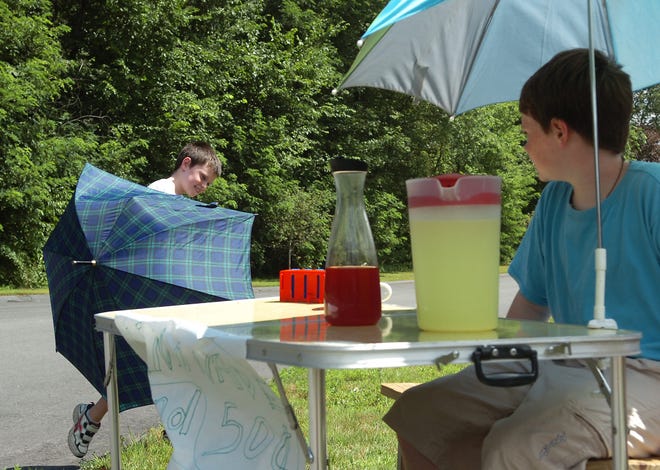 Aidan Connor, 9, left, of Medway, rejoins his brother Sean, 11, right, at their lemonade stand on Waterview Drive after the umbrella he was using to shield himself from the sun blew away. They were selling lemonade and fruit punch to earn some extra spending money for the summer.