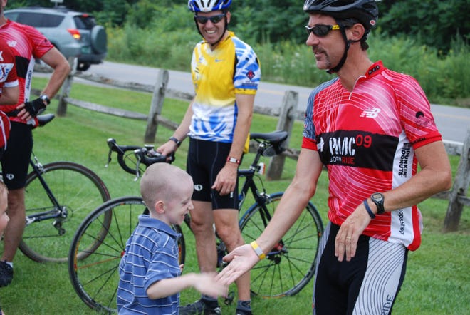 Christopher Grimes slaps hands with his uncle Ed McGovern, who was riding to raise money for neuroblastoma research last summer.