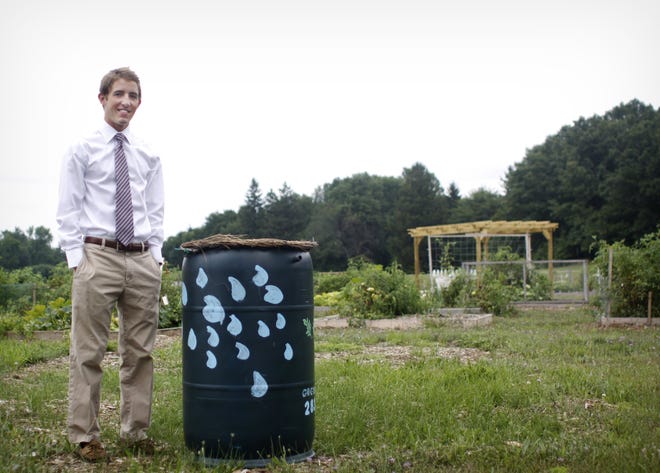 Mitchell Rhein stands outside Park Township's community garden on Thursday, August 5. The water collected in the rain barrel will be used to water the garden.