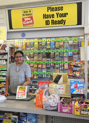 Bhagti Patel shows a smaller version of the sign that hangs above the cash register in Oak Street Convenience in Brockton, seen on Monday, August 8, 2011, reminding customers that they must be at least 18 years old to purchase tobacco products.