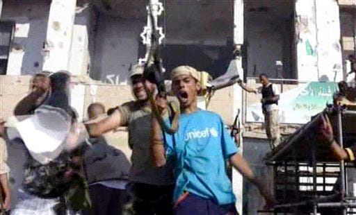 Rebel fighters react after entering Moammar Gadhafi's compound in Tripoli in this image taken from TV on Tuesday Aug. 23, 2011. The sprawling complex, heavily damaged by NATO airstrikes, is the most defining symbol of Gadhafi's nearly 42-year rule and its fall, a day after the rebels swept into the Libyan capital with stunning speed, comes as the opposition faced pockets of resistance and fighting rocked the capital.