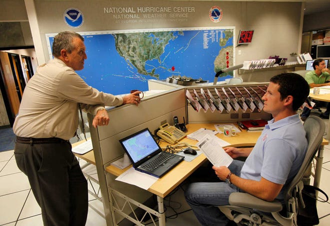 National Hurricane Center director Bill Read, left, talks with meteorologist Wallace Hogsett, Monday, Aug. 22, 2011 at the National Hurricane Center in Miami. As of the 5:00 p.m. advisory the center of Hurricane Irene was estimated to be near latitude 19.5 North, longitude 68.6 West, moving toward the West-Northwest near 13 MPH. (AP Photo/Wilfredo Lee)