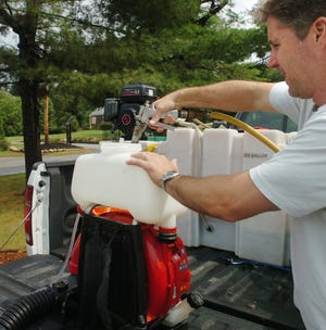 Tom Norton of Combat Pest Control refills a dispenser with Mosquito Barrier, a garlic-based mosquito repellent, in Hanover, Friday, July 8, 2011.