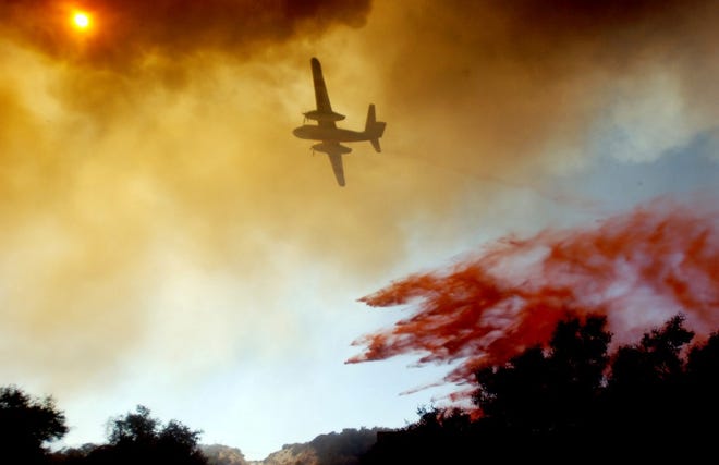 A fire-fighting aircraft drops fire retardant over a neighborhood threatened by the Hills Fire burning Friday near Hesperia, Calif. A fast-moving wildfire erupted Friday on the main interstate between Southern California and Las Vegas, forcing evacuations of 1,500 homes, temporarily closing the freeway to holiday weekend traffic and surging through hundreds of acres of desert brush. (The Associated Press)
