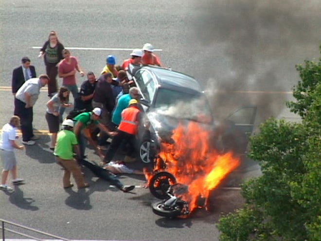 In this Monday, Sept. 12, 2011 image taken from video, a group of people tilt a burning BMW up to free Brandon Wright, on his back on the ground, who was pinned underneath after he collided with the car while riding his motorcycle on U.S. 89 in Logan, Utah. Authorities said Wright was riding his motorcycle near the Utah State University campus in Logan when the 21-year-old collided with the BMW that was pulling out of a parking lot. Tire and skid marks on the highway indicate that Wright laid the bike down and slid along the road before colliding with the car, Assistant Police Chief Jeff Curtis said. (AP Photo/Chris Garff)