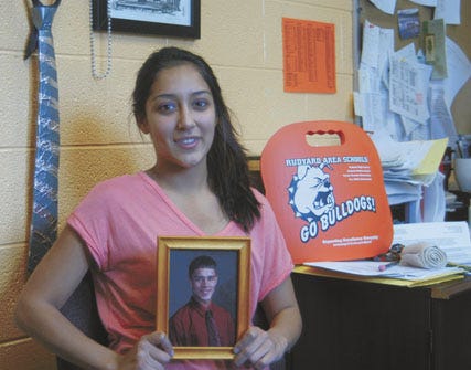 Seventeen-year-old Brittany Rogers of Rudyard smiles while holding her big brother John’s photograph in the high school principal’s office. Brittany received a kidney transplant from John in May, and returned to Rudyard High School for her senior year this fall.